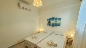 A hotel room with two beds, a wall-mounted air conditioner, a ceiling light, and a wall art piece. - Cosy Villa Walking Distance to a Mykonian Beach (Mykonos)