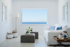 A minimalist living room with a large window, white furniture, and a view of the sea. - The Mykonian Escape (Mykonos)