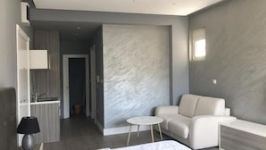 Moderni hotellihuone, jossa on sänky, pieni pyöreä pöytä, sohva ja seinään integroitu penkki.