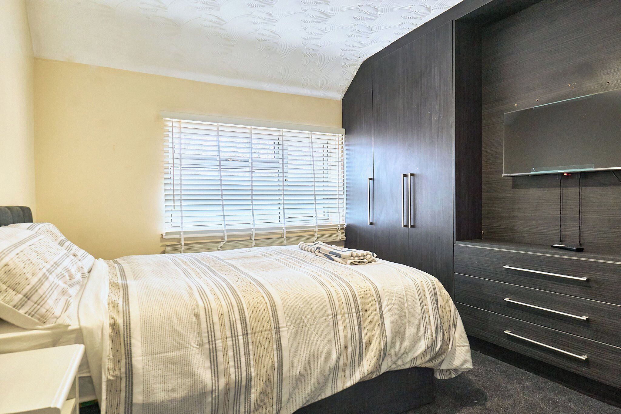 Un dormitorio con cama, ventana con persianas, armario oscuro y escritorio.