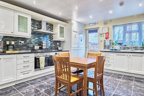 A modern kitchen with white cabinets, a black tiled backsplash, a wooden dining table, and a window with a view.