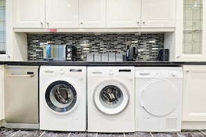 A kitchen with white cabinets, a tiled backsplash, and two Bosch washing machines.