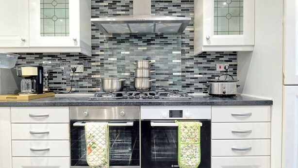 A kitchen with white cabinets, a tiled backsplash, a stove, and two ovens. - House Sleeps 8 - Free Parking & Wifi (Birmingham)