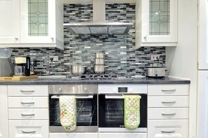 A kitchen with white cabinets, a tiled backsplash, a stove, and two ovens.