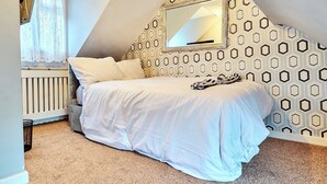 A bedroom with a bed, a window with curtains, a radiator, and a geometric-patterned wall. - House Sleeps 8 - Free Parking & Wifi (Birmingham)