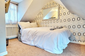 A bedroom with a bed, a window with curtains, a radiator, and a geometric-patterned wall.