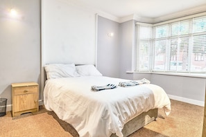 A bedroom with a bed, a nightstand, a window with blinds, and a carpeted floor.