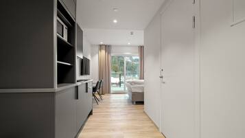 A modern hotel room with a kitchenette, a bed, a seating area, and a large window.