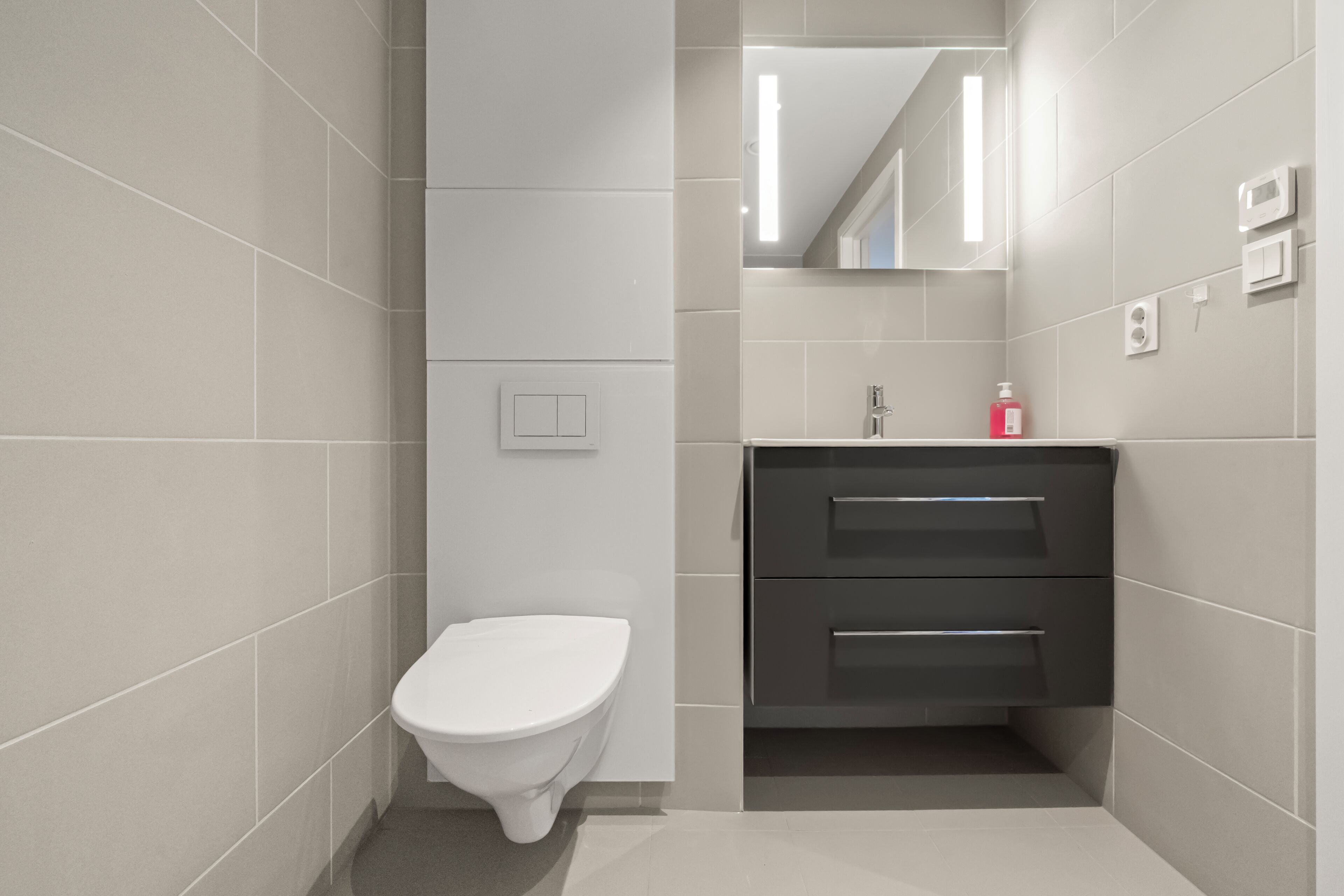 Un baño moderno con inodoro, lavabo con espejo y un interruptor de luz en la pared.