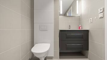 Un baño moderno con inodoro, lavabo con espejo y un interruptor de luz en la pared.