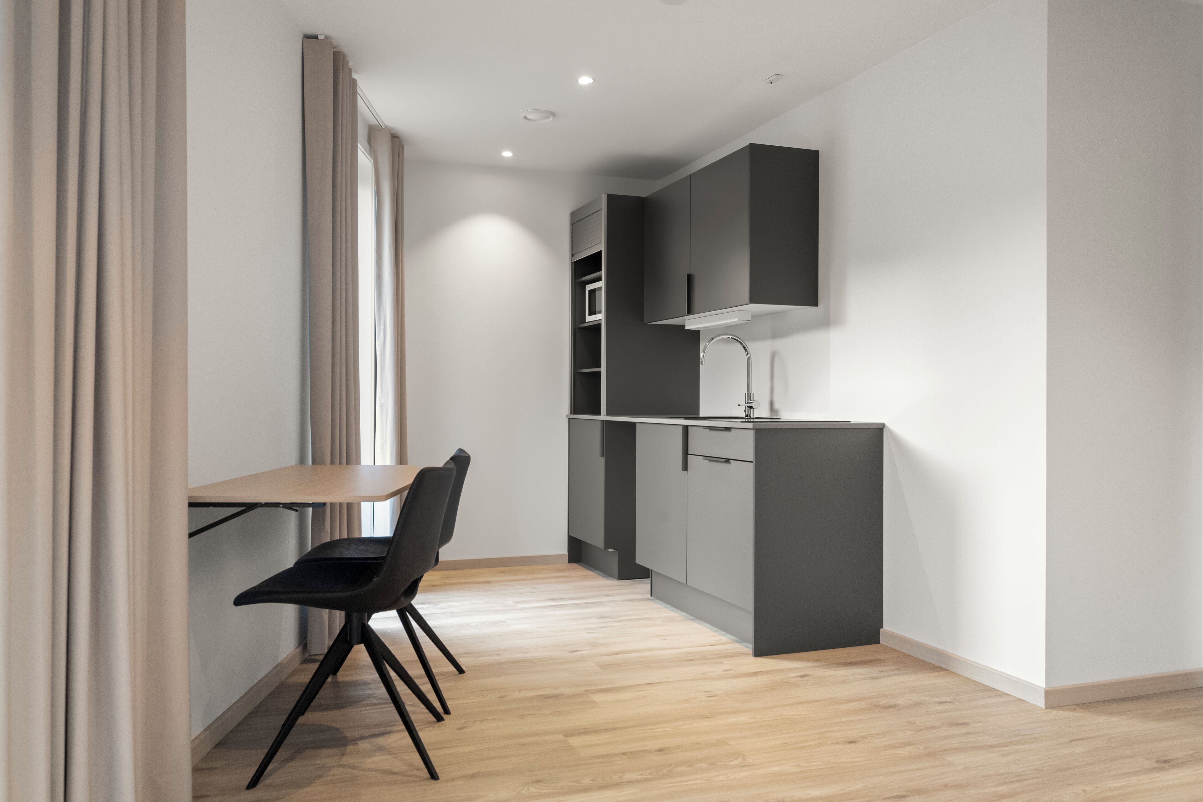 A modern kitchen with grey cabinets, a wooden dining table, and black chairs.