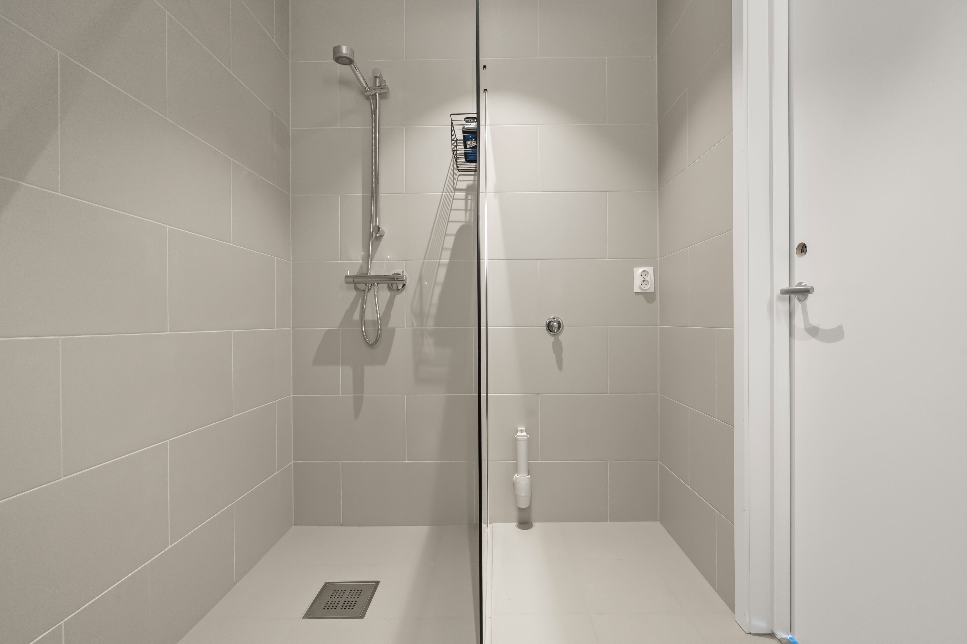 A modern shower with a glass door, a handheld showerhead, and a wall-mounted control panel.