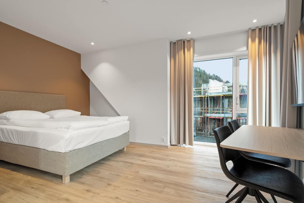 A modern hotel room with a bed, a dining table, and a view of a balcony.