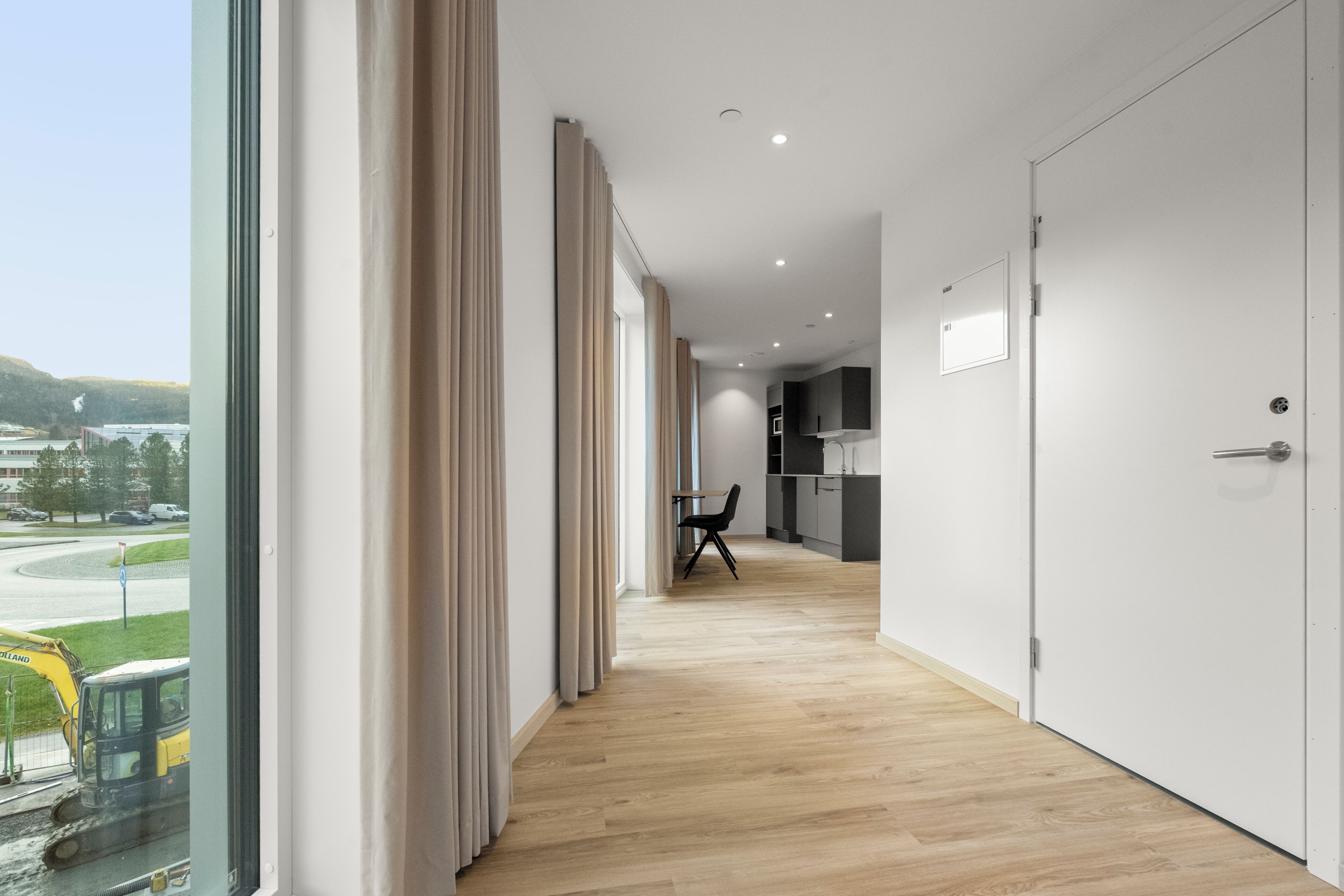 A modern hotel corridor with a view of a construction site, a dining area, and a kitchen.