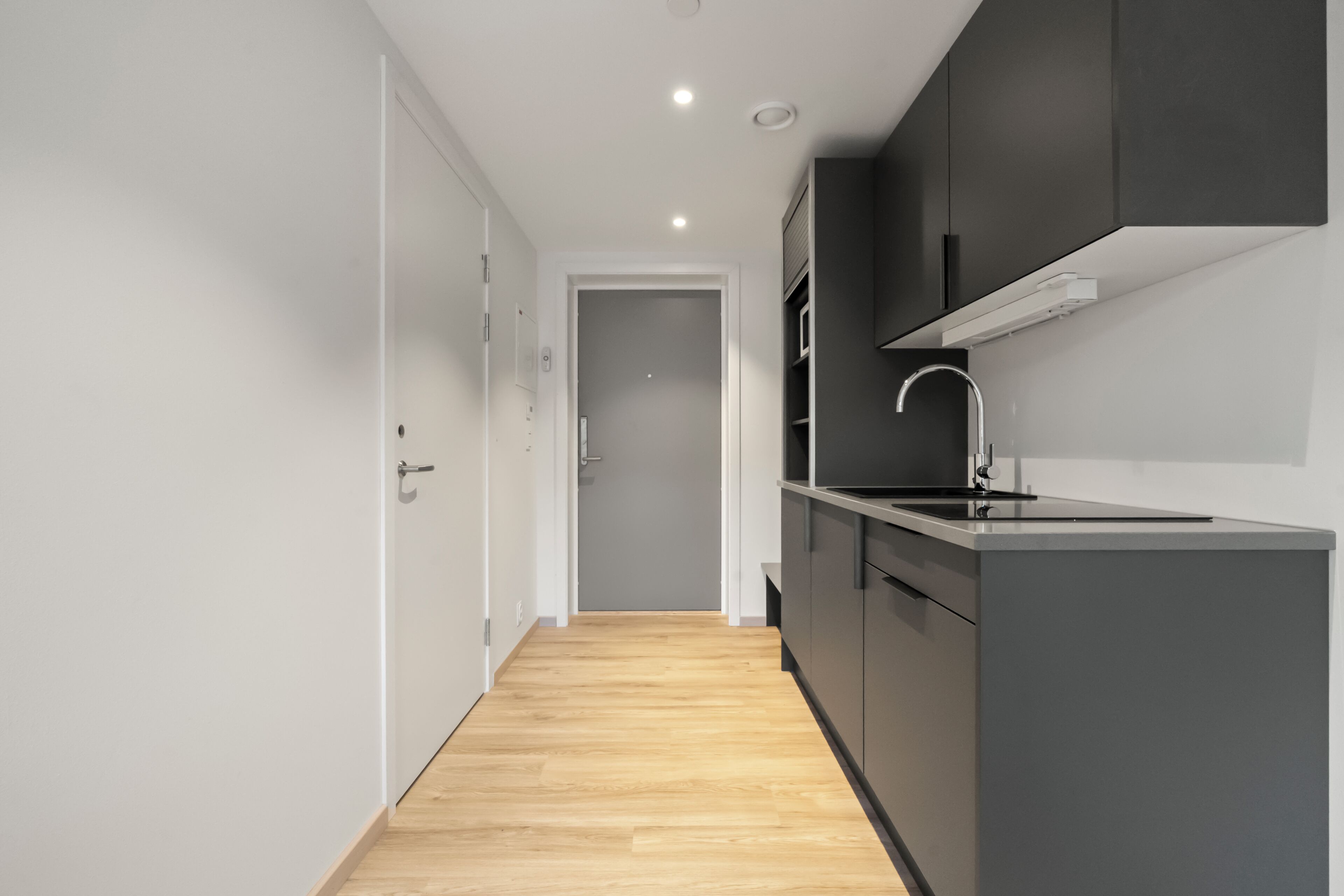 Una cocina moderna con armarios oscuros, piso de madera y una puerta blanca.