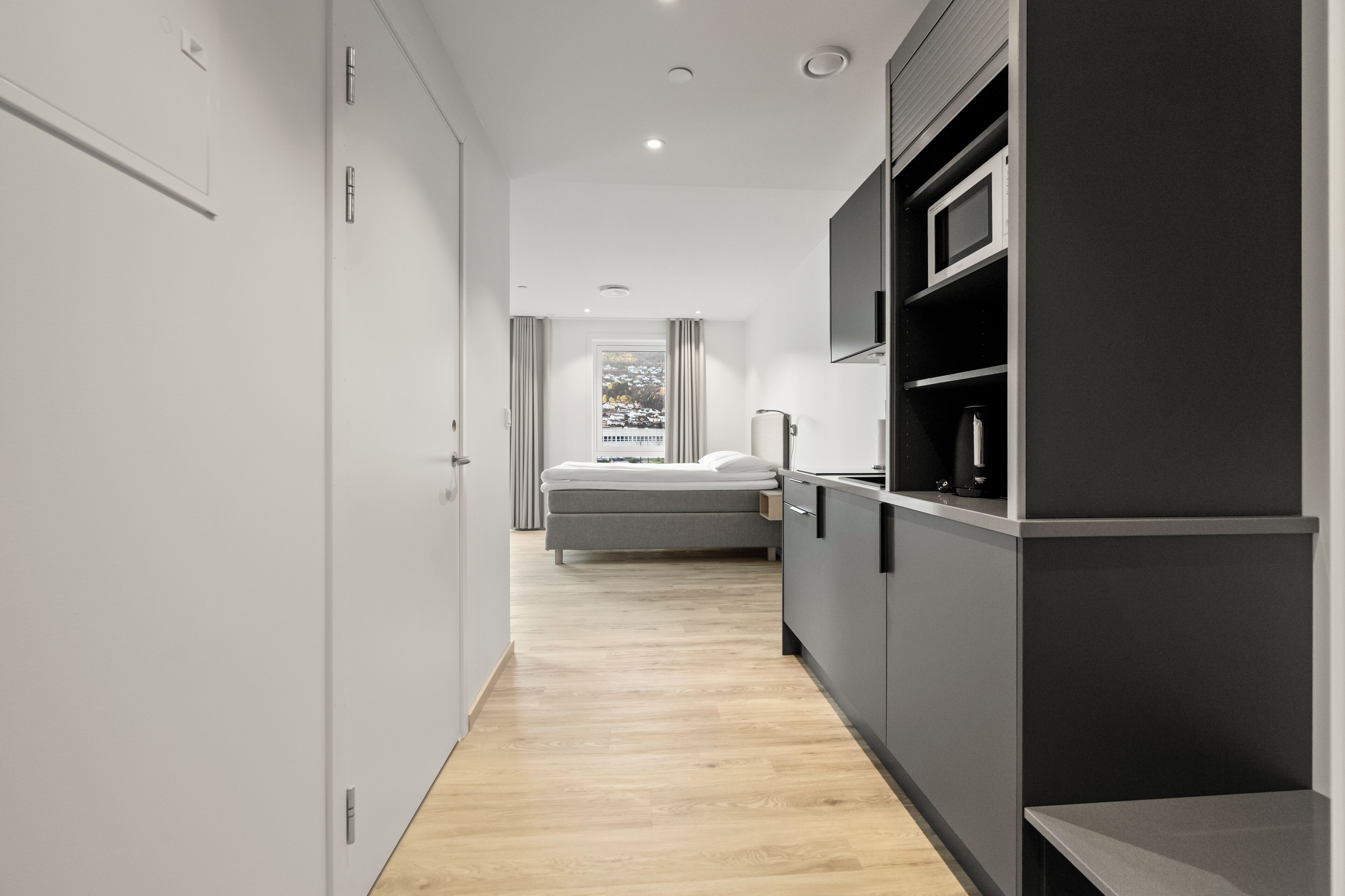 Une chambre d’hôtel moderne avec un plancher en bois, un lit, un coin cuisine intégré et une fenêtre donnant sur un paysage agréable.