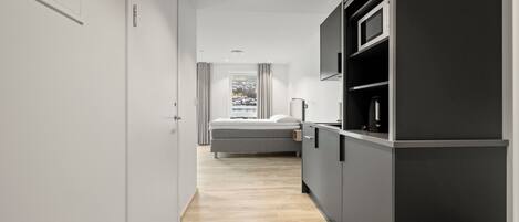Une chambre d’hôtel moderne avec un plancher en bois, un lit, un coin cuisine intégré et une fenêtre donnant sur un paysage agréable.