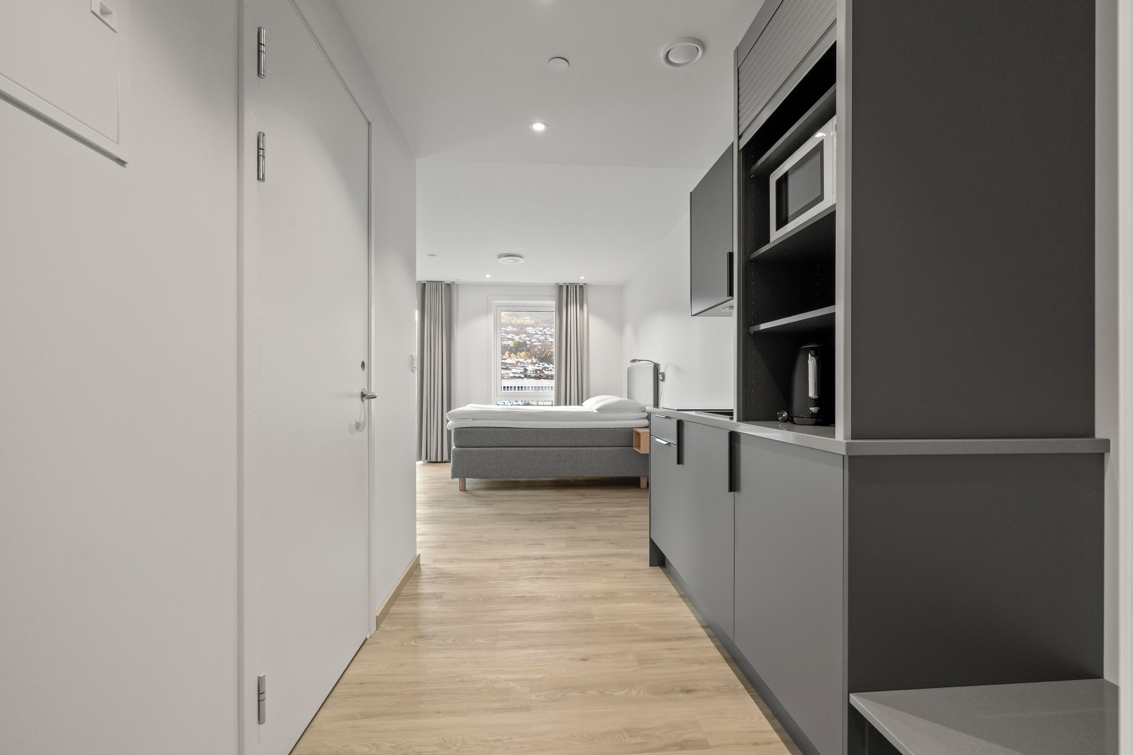A modern hotel room with a wooden floor, a bed, a wardrobe, and a window with curtains.