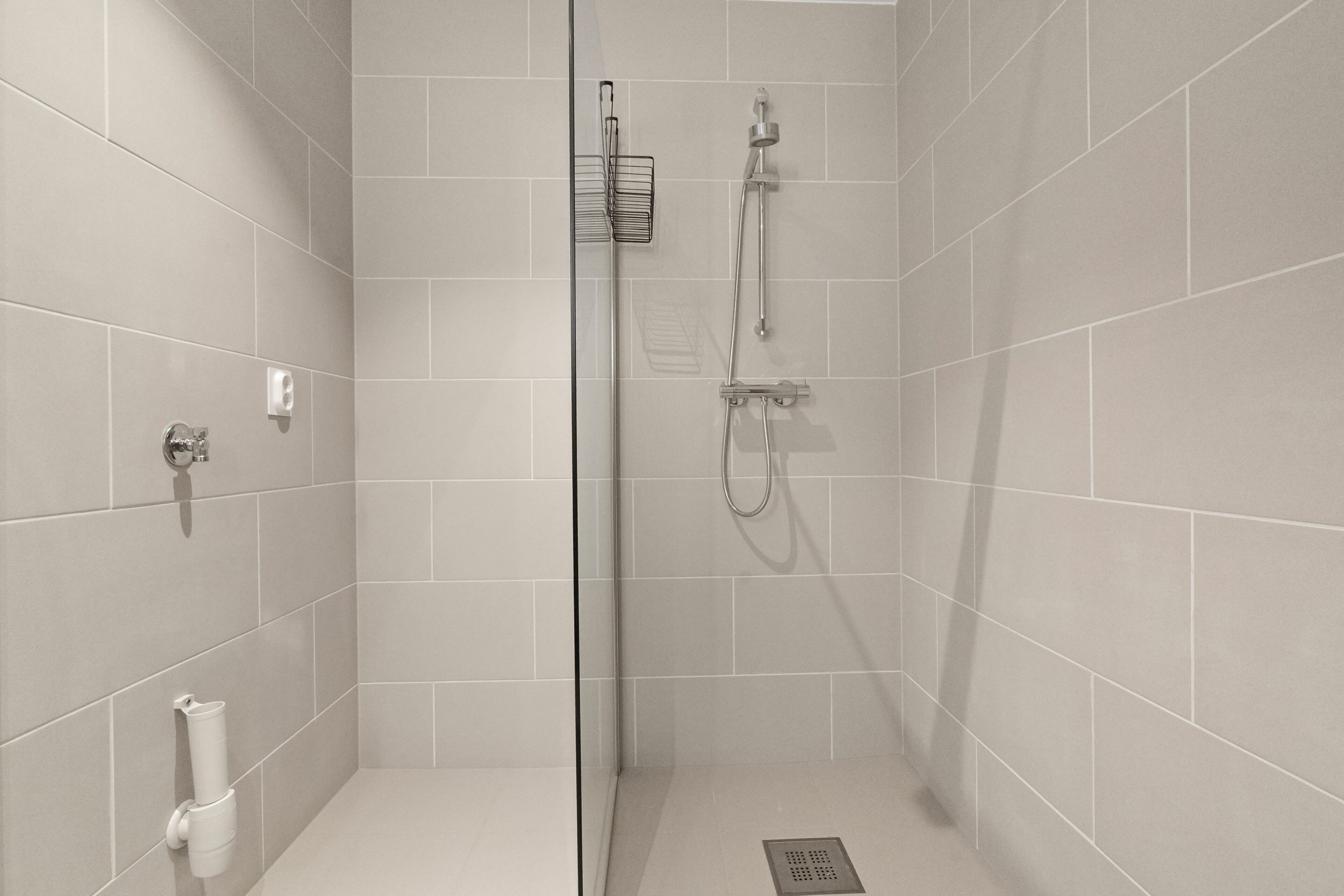 A modern shower with a glass door, a handheld showerhead, and a wall-mounted faucet.