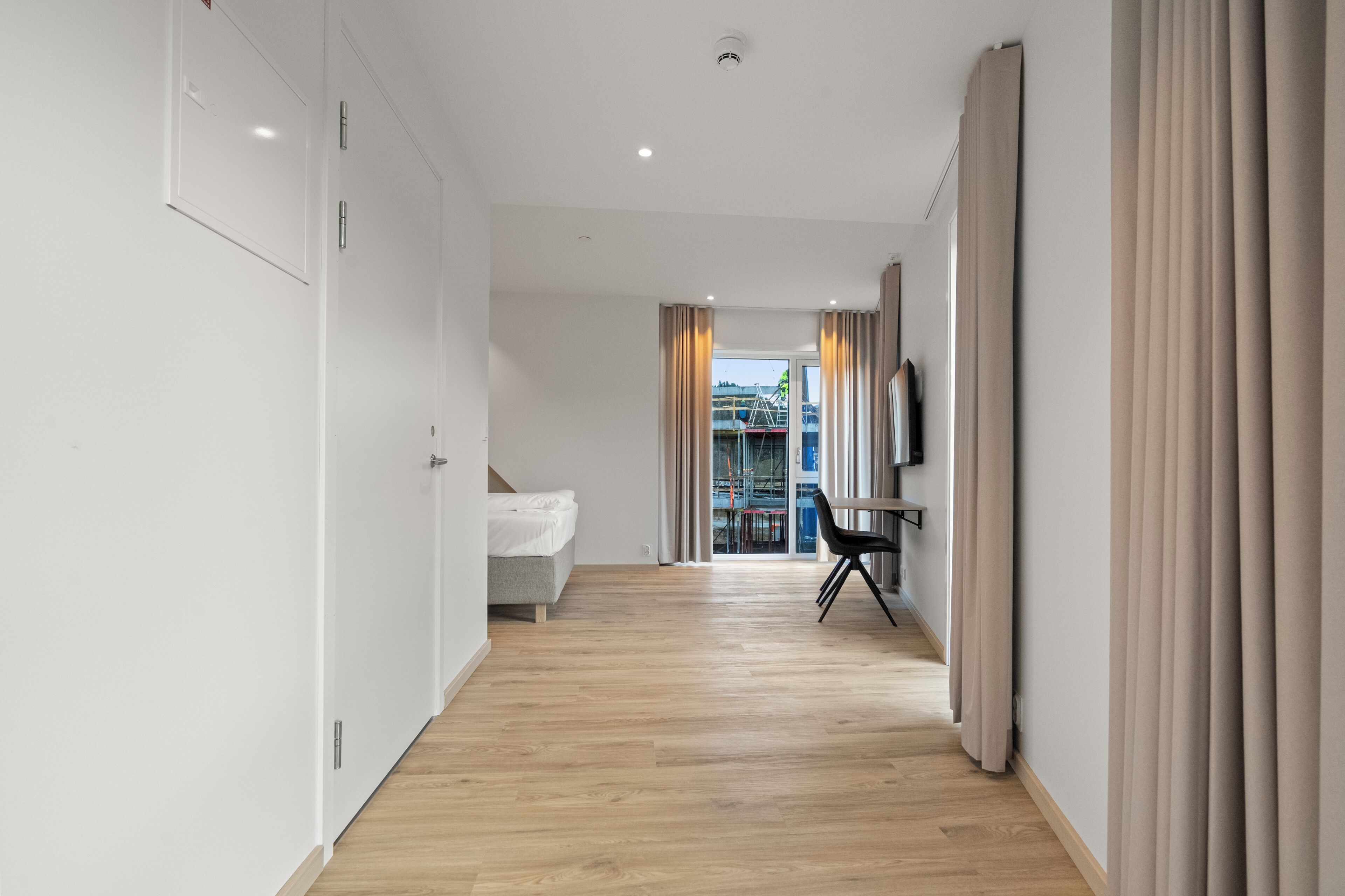 Une chambre d’hôtel moderne avec un plancher en bois, un lit, un bureau et une télévision.