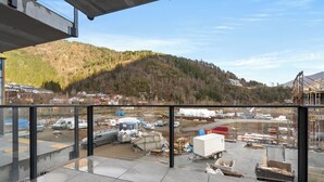 Una obra en construcción con vehículos y materiales, un paisaje montañoso al fondo y cielo despejado.