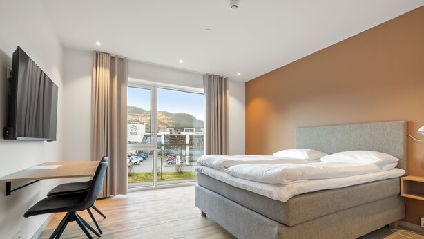 Un hotel moderno con cama, escritorio, silla y un amplio ventanal que ofrece vistas a la ciudad.