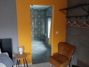 A room with a bed, a chair, a small table, a coat rack, and a patterned shower curtain. - Le Salmon, an authentic 19th-century hotel renovated as a B&B in Neufchâteau (Neufchâteau)