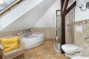 A bathroom with a bathtub, toilet, shower, and a wicker chair with a yellow pillow. - Traditional Family Apartment | Workspace (Poznań)