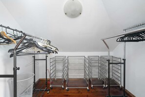 Et værelse med loftlampe, metalstativ med knager og metalreoler.