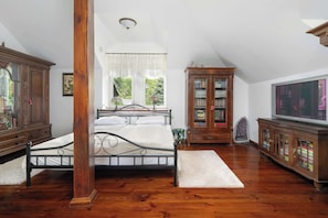 A bedroom with a bed, wooden cabinets, a television, and a window with a view of greenery. - Traditional Family Apartment | Workspace (Poznań)