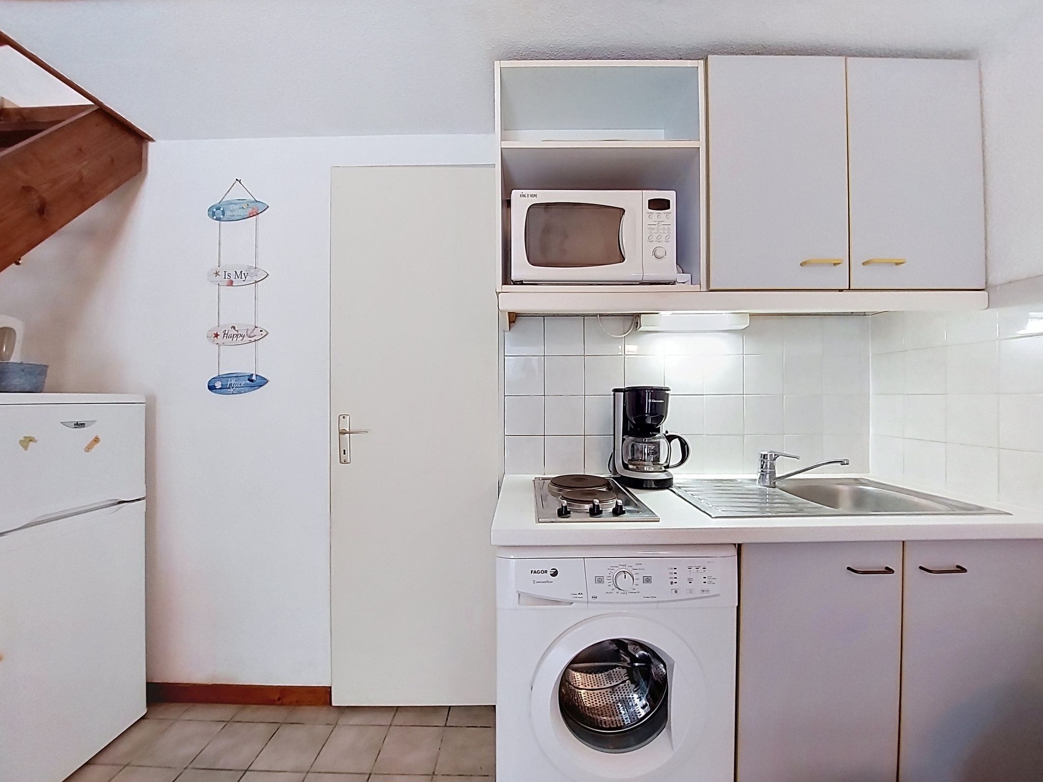Een kleine keuken met een magnetron, koffiezetapparaat en wasmachine.