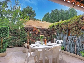 An outdoor patio with a round table set for two, surrounded by white plastic chairs. - Hameau de Talaris by Interhome (Les Mathes)