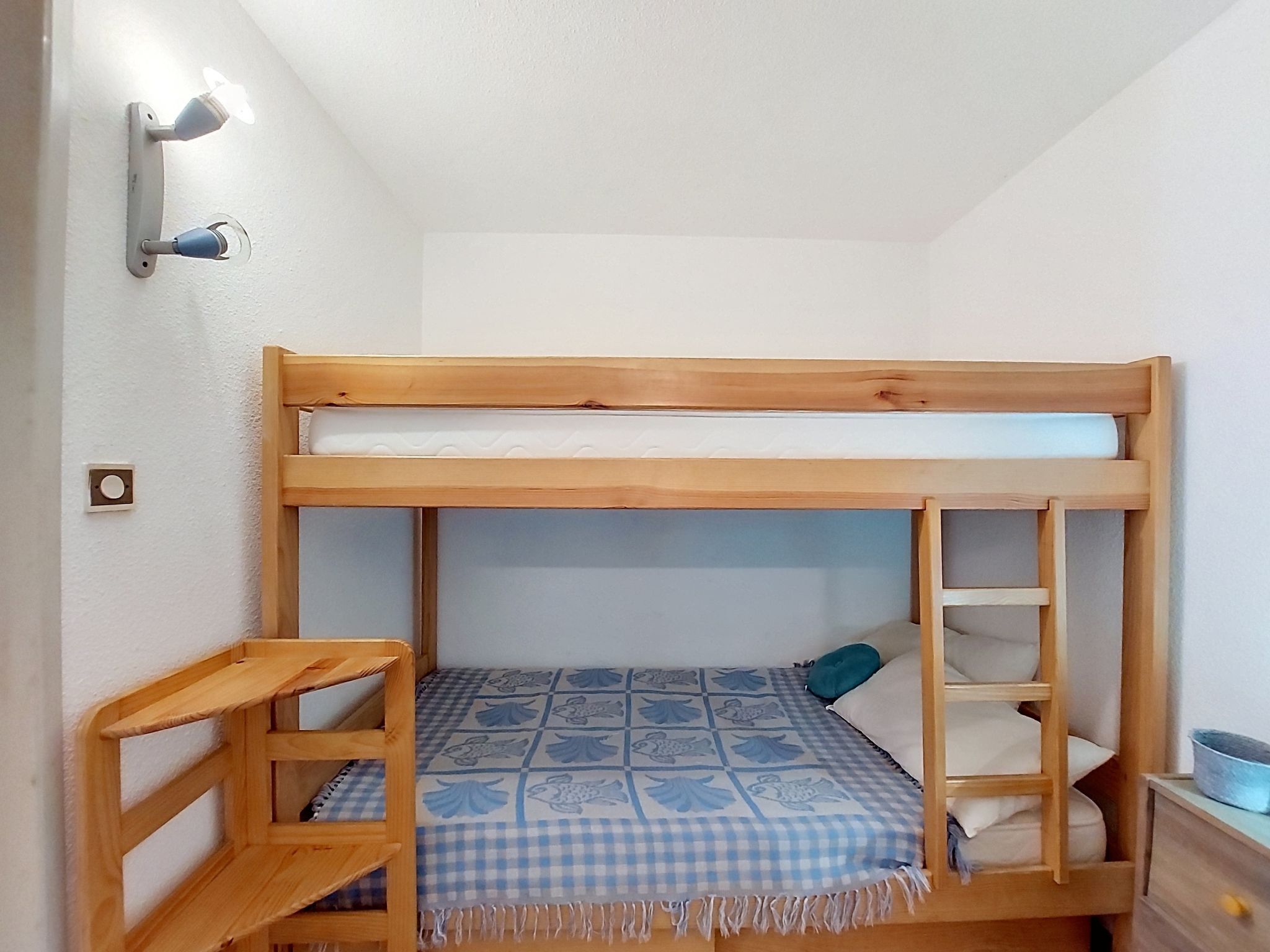 En våningssäng med ett rutigt överkast, en trästege och en liten hylla.