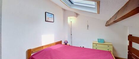 A bedroom with a skylight, wooden bed frame, a bedside table, a lamp, and a dresser.