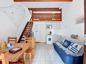 Ein gemütlicher Wohnraum mit Esstisch aus Holz, einer Couch mit marineblauen Kissen, einer Waschmaschine, einer Mikrowelle und einer Treppe.