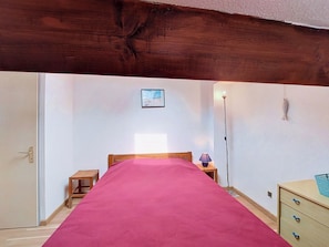 Een slaapkamer met een bed, nachtkastje, lamp, dressoir en een klein tafeltje.