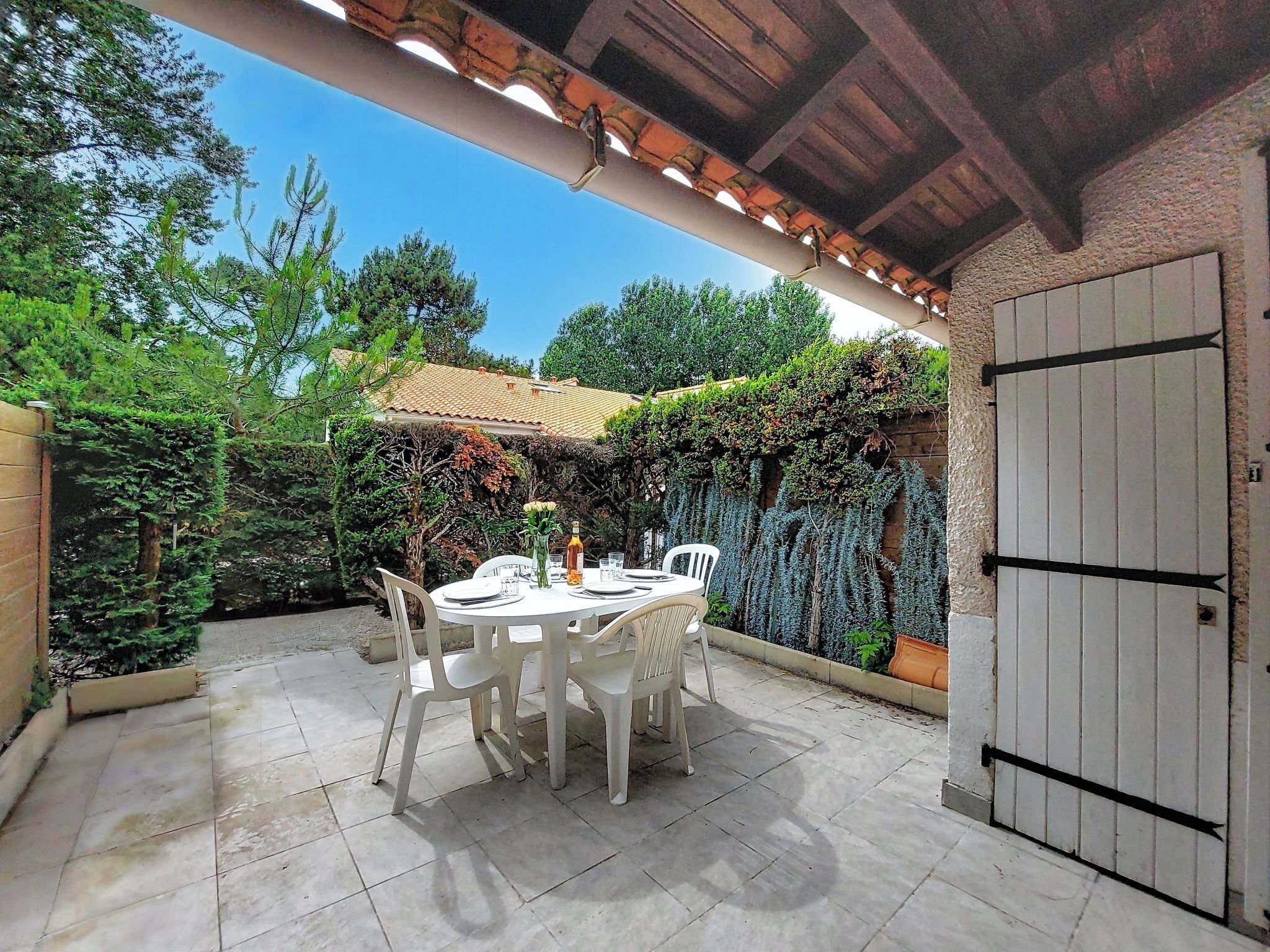 An outdoor patio with a table and chairs, a tiled floor, and a wall with climbing plants.