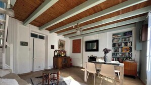 A spacious living room with a high ceiling, wooden beams, a dining area with chairs, a bookshelf, and a fireplace. - Le Nid du Matelot (Saint-Vaast-la-Hougue)