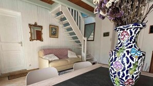 A room with a white staircase, a beige sofa, a white chair, a patterned vase, and a door. - Le Nid du Matelot (Saint-Vaast-la-Hougue)
