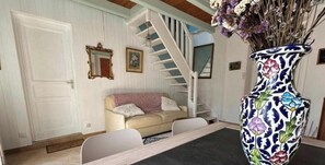 Une pièce avec un escalier blanc, un canapé beige, une chaise blanche, un vase à motifs et une porte.