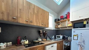 A kitchen with wooden cabinets, a microwave, a refrigerator, and a coffee machine. - Le Nid du Matelot (Saint-Vaast-la-Hougue)
