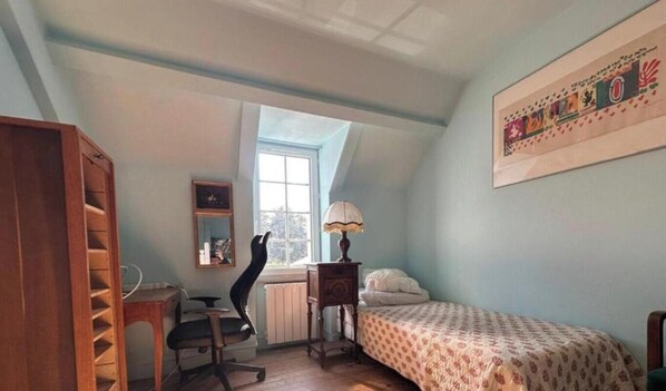 Ein Zimmer mit einem Bett, einem Schreibtisch, einem Stuhl, einem Heizkörper und einem Fenster.