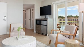 Un salon moderne doté d’un téléviseur à écran plat, d’un coin repas avec une table et des chaises, et offrant une vue sur une piscine et un espace verdoyant à l’extérieur.