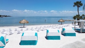 Un hotel frente a la playa con sillas de playa blancas y azules, sombrillas de paja y una vista despejada del mar.