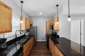A modern kitchen with wooden cabinets, stainless steel appliances, and pendant lighting. - Modern 2br Townhome in Prime Location (Clarksville)