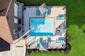An aerial view of a rooftop pool area with a rectangular pool, four lounge chairs, and two umbrellas. - Modern 2br Townhome in Prime Location (Clarksville)
