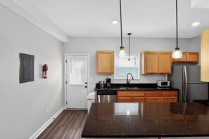 A modern kitchen with wooden cabinets, a stainless steel refrigerator, a microwave, and a large island with a dark countertop. - Modern 2br Townhome in Prime Location (Clarksville)