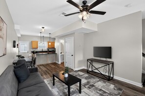 A modern living room with a sofa, coffee table, TV, and ceiling fan. - Relaxing 2BR Stay with Community Perks (Clarksville)