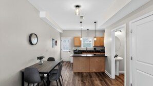 Una cocina moderna con armarios de madera, una isla central, luces colgantes y una zona de comedor con mesa y sillas.