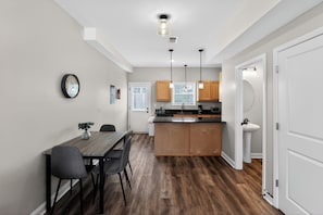 A modern kitchen with wooden cabinets, a central island, pendant lights, and a dining area with a table and chairs. - Relaxing 2BR Stay with Community Perks (Clarksville)